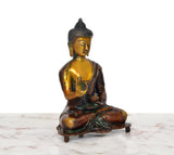 Brass Buddha statue seated, Abhaya mudra hand raised, golden highlights on dark robe