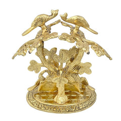 Gold-tone Radha Krishna idol under tree, wide view showing birds overhead and tree trunk