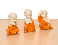 Close view of three orange-robed monk Buddha resin figures, seated and clasped hands
