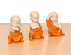 Close view of three orange-robed monk Buddha resin figures, seated and clasped hands