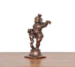 Copper dancing Bal Krishna figure holding laddu, side view on round base