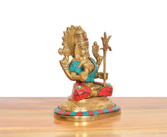 Brass seated goddess statue shown from front-right: gold crown, teal attire, red skirt, raised hand.