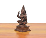 Copper Lakshmi Maa idol from the side, seated with multiple arms holding small staffs