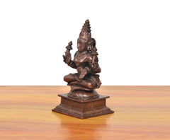Copper Lakshmi Maa idol from the side, seated with multiple arms holding small staffs