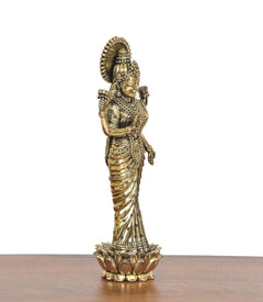 Brass Lakshmi idol in profile, holding ornaments, standing on lotus petals