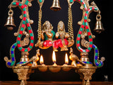 Close-up of Radha Krishna swing idol and hanging diya lamps, colorful arch supports