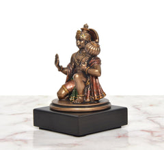 Resin Hanuman idol side view, seated posture with raised hand, multicolor clothing.