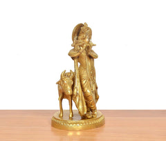 Brass Krishna playing flute beside cow idol, seen from side, golden finish