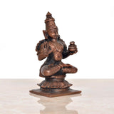 Copper Dhanvantari statue three-quarter view, holding small pot-like item, seated lotus