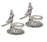 Close view of two metal parrot diyas with leaf-like tails and raised oil cups
