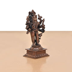 Copper Lord Kal Bhairav idol shown from an angle, holding weapons, on engraved base