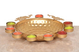 Gold peacock urli bowl with textured finish and tea light cups with red, green, and orange wax