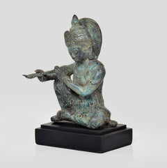 Bronze Krishna Sitzfigur mit Flöte, seitlicher Blick, türkisgrüne Patina, schwarzer Sockel