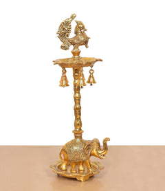 Golden metal peacock diya stand with hanging bell-like lamps and elephant base