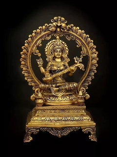 Brass Saraswati statue seated on elevated plinth, ornate circular halo and raised hands