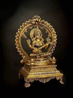 Brass Saraswati statue seated on pedestal, circular halo behind, one hand holding veena