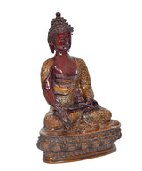 Seated Buddha idol angled view, dark red torso and gold patterned sash, ornate base