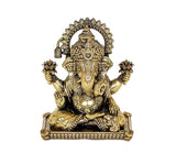 Brass Ganesha idol close-up, detailed face, raised arms, and circular halo