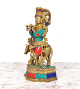 Side view of brass Krishna playing flute idol with cow companion, multicolor accents