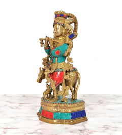 Side view of brass Krishna playing flute idol with cow companion, multicolor accents