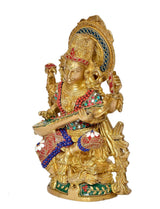 Brass Saraswati idol side view, seated goddess holding flute, ornate jewelry and patterned base