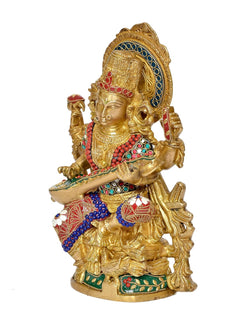 Brass Saraswati idol side view, seated goddess holding flute, ornate jewelry and patterned base