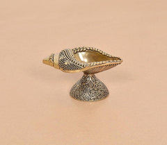 Brass conch oil diya lamp standing on carved pedestal, open shell bowl in bronze tone