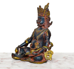Side view of Kuber brass murti, seated with raised left hand and gold ornaments