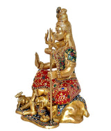 Side view brass Shiva murti, seated figure holding trident, red-green decorated clothing