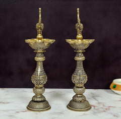 Brass peacock oil lamp pair showing tall stems, tiered base, and central finial.