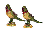 Two iron parrot statues perched on gold bases, green, gold, and dark red