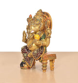 Brass Ganesha statue shown from side, seated on chowki with colorful meenakari work
