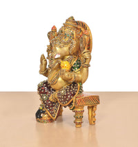 Brass Ganesha statue shown from side, seated on chowki with colorful meenakari work
