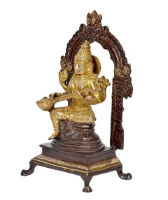 Brass seated Saraswati idol in side view, holding items and seated on pedestal