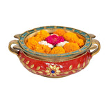 Brass urli bowl with red enamel finish, blue border, and marigold flowers inside