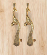 Two brass peacock door handles mounted on light wood, golden tone