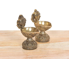 Two brass diya shankh oil lamp stands with carved feet and embossed bowl patterns