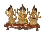 Lakshmi, Ganesh, and Saraswati brass-gold statue set on ornate brown base platform