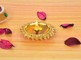 Golden metal oil diya lamp with ornate rim and lit wick in center