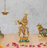 Metal Lord Krishna sculpture playing flute, gold finish with red and blue base details