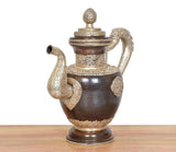 Dark brown brass teapot with curled left spout, raised medallions, and domed lid