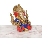Brass Ganpati idol angled view, blue-red patterned clothing with gold hands and crown