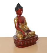Buddha statue from front-left angle, red face and hands, gold robe, seated on ornate base