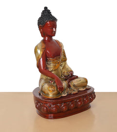 Buddha statue from front-left angle, red face and hands, gold robe, seated on ornate base