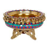 Decorative brass urli with teal-red patterned border, dangling bells, and 3 feet