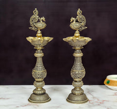Brass peacock oil lamp pair with ornate stand and central bowl, decorative detail.