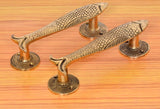 Golden brass fish door handles with cylindrical posts on a wooden surface.