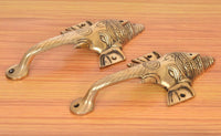 Two brass Ganesha face door handles laid on wooden surface, curved pull grips
