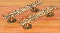 Ornate brass door pull handles pair with curved backplates on wood