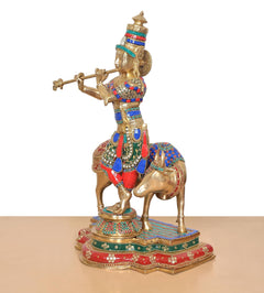 Side view of Brass Lord Krishna on cow idol, colorful outfit and crown
